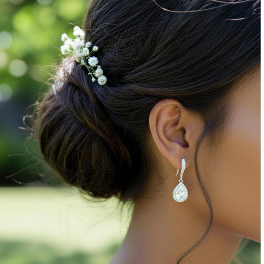 Close-up of a woman's hair with a bun and small flowers, wearing elegant earrings outdoors.