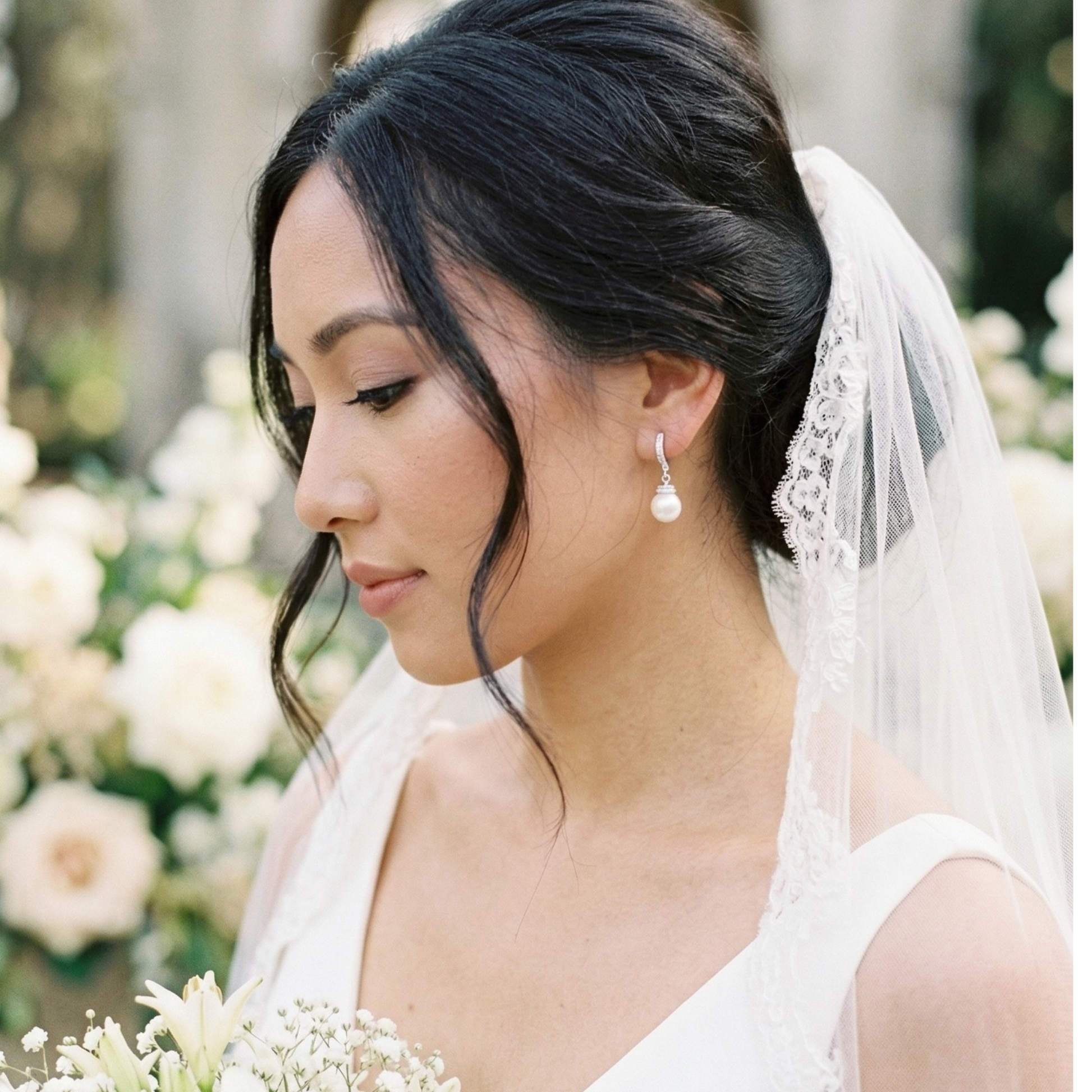 Close-up of a woman's ear wearing an elegant silver pearl drop earring featuring a curved hook accented with small sparkling stones and a round white pearl.