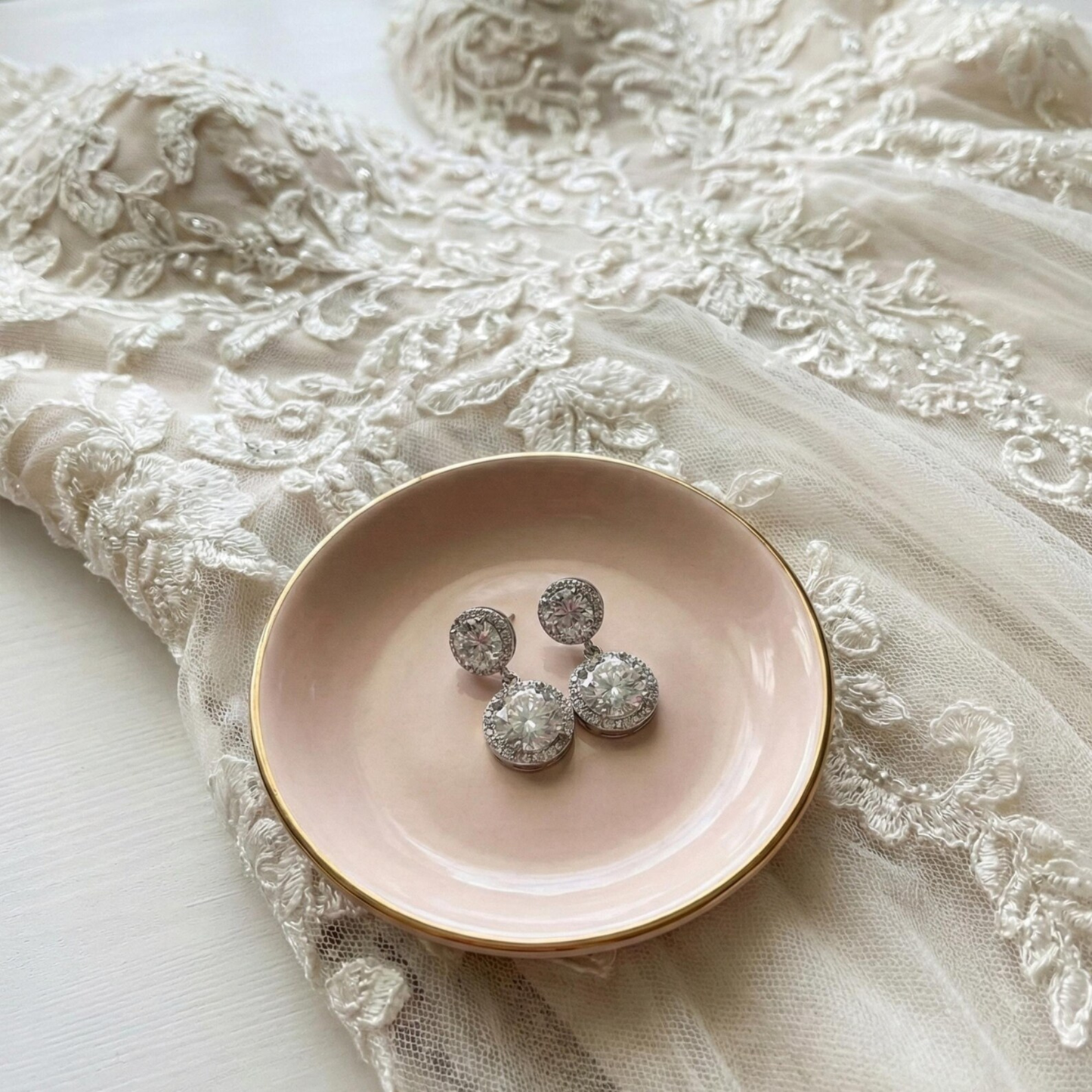 Silver earrings on a pink plate with lace fabric in the background