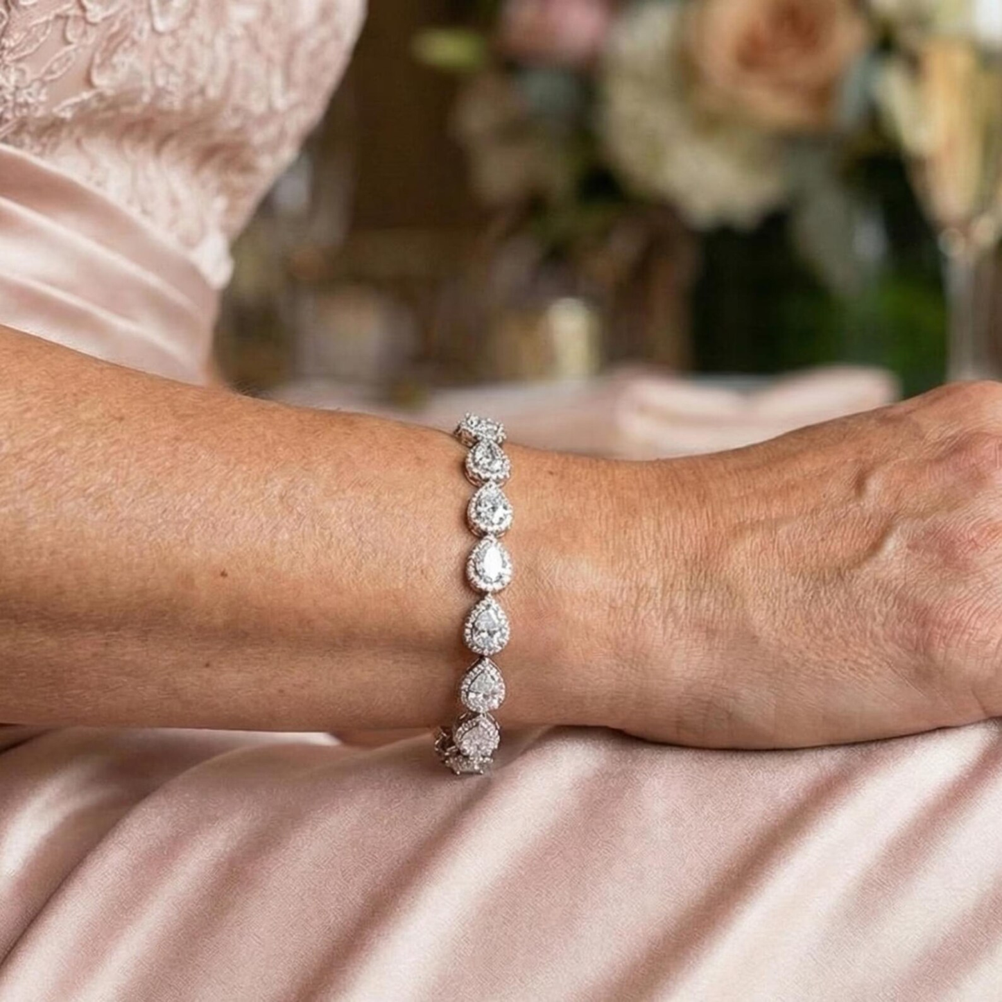 Close-up of a faux diamond bracelet on a Mother of the bride's wrist with a blurred floral background