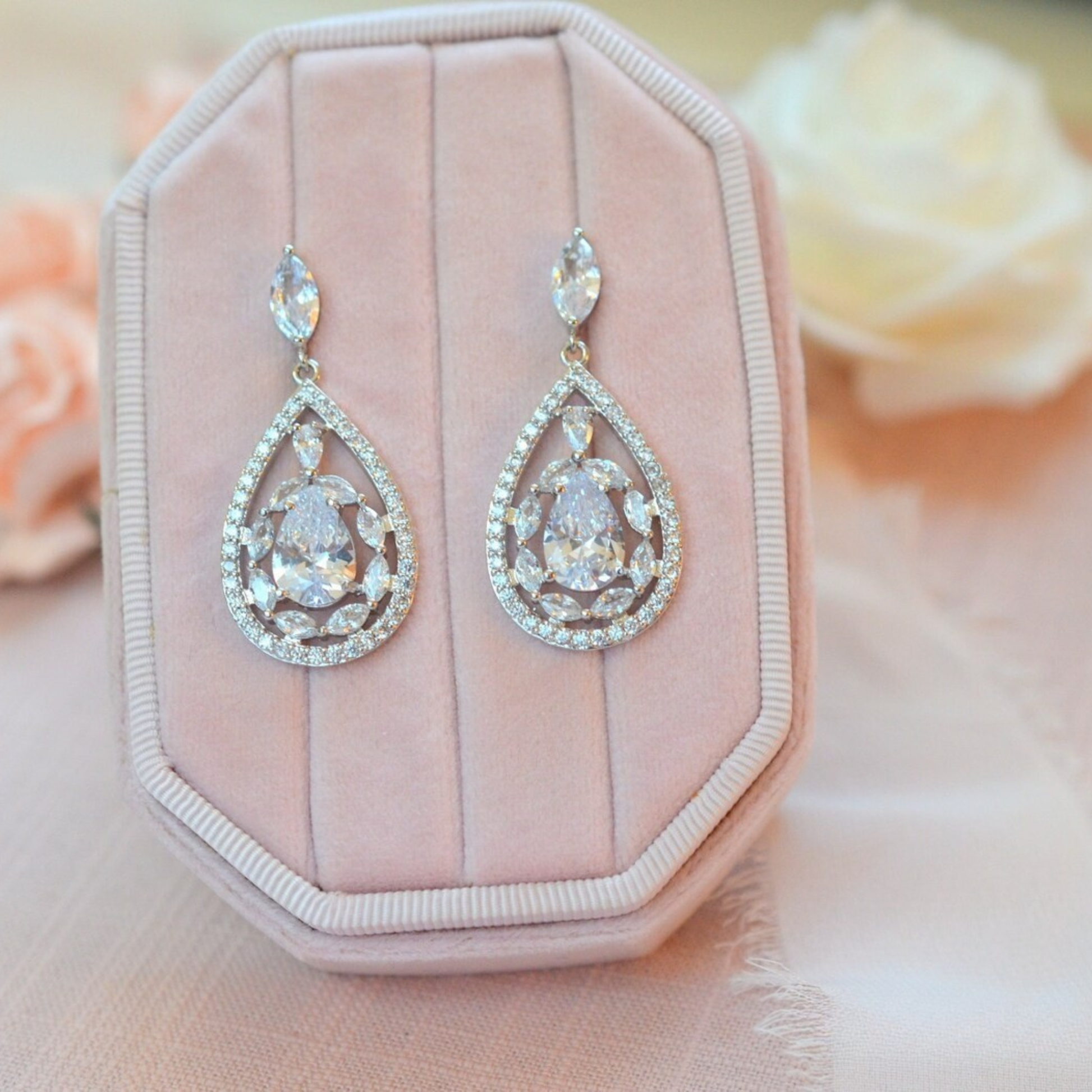 Teardrop-shaped earrings on a pink jewelry box with flowers in the background