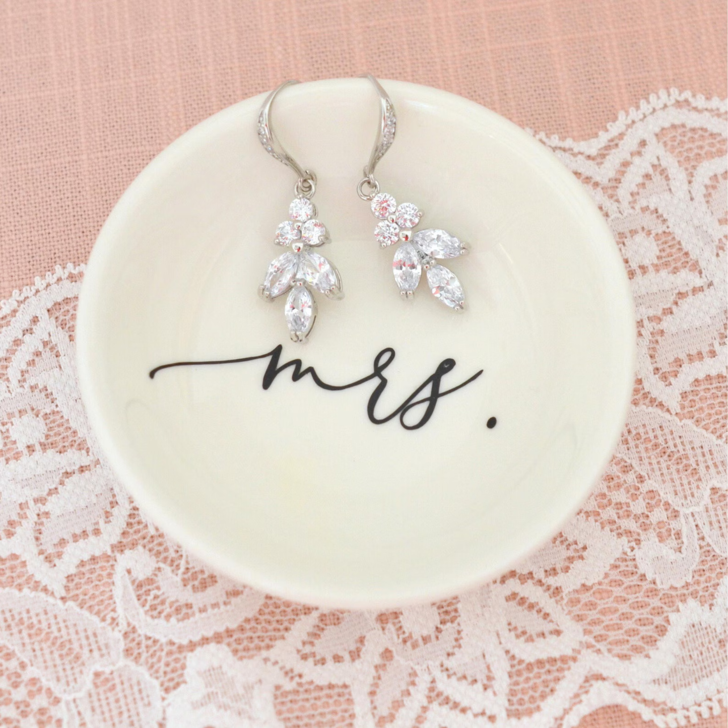 Pair of silver earrings on a 'mrs.' dish with lace background