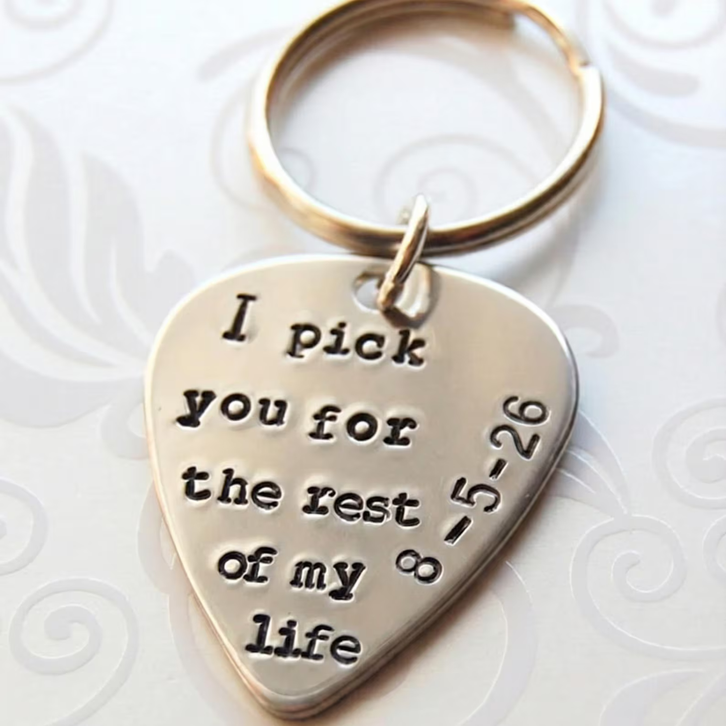Hand-stamped guitar pick keychain with engraved text I pick you on a white background