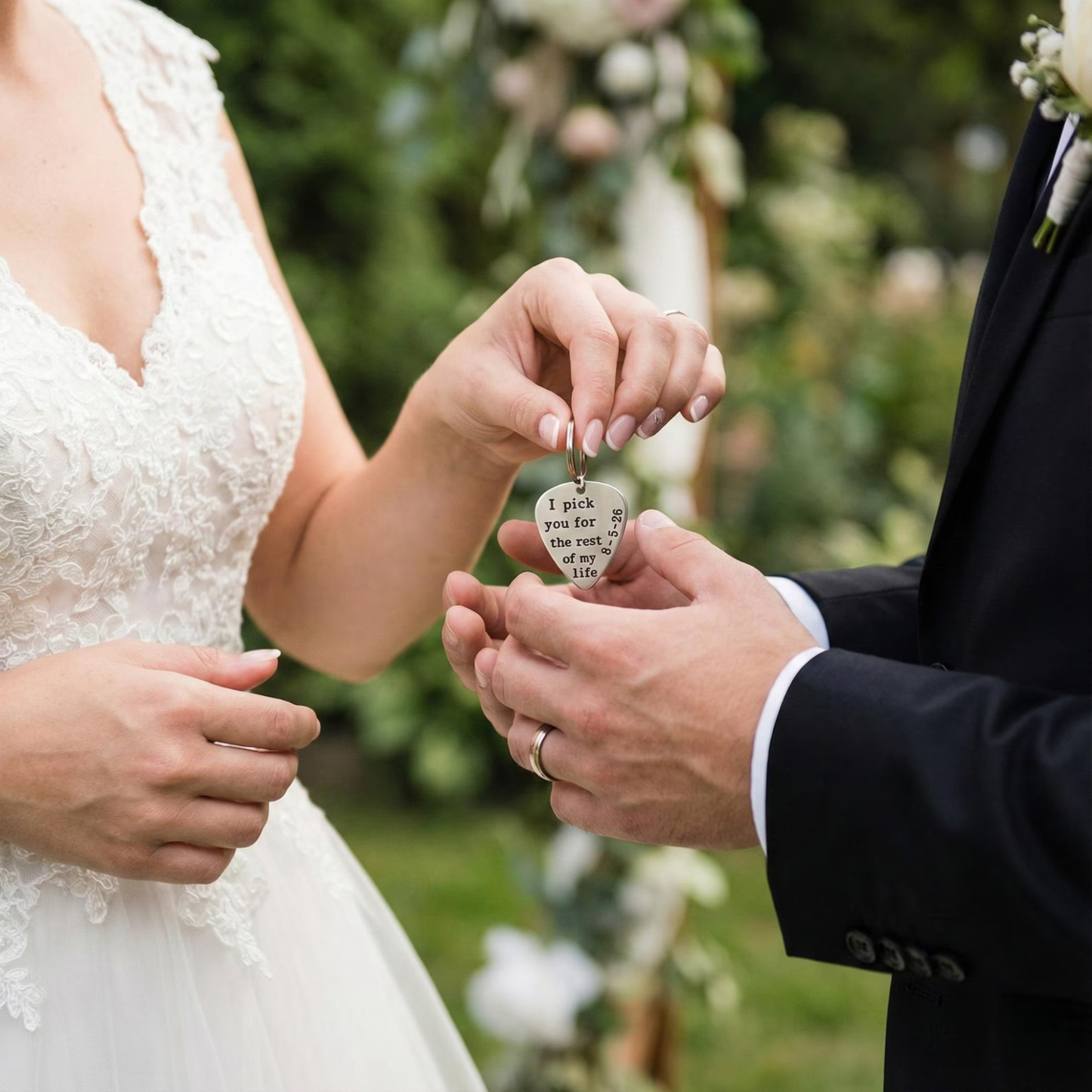 Bride giving groom a custom guitar pick keychain with a message-I pick you for the rest of my life, surrounded by greenery and flowers.